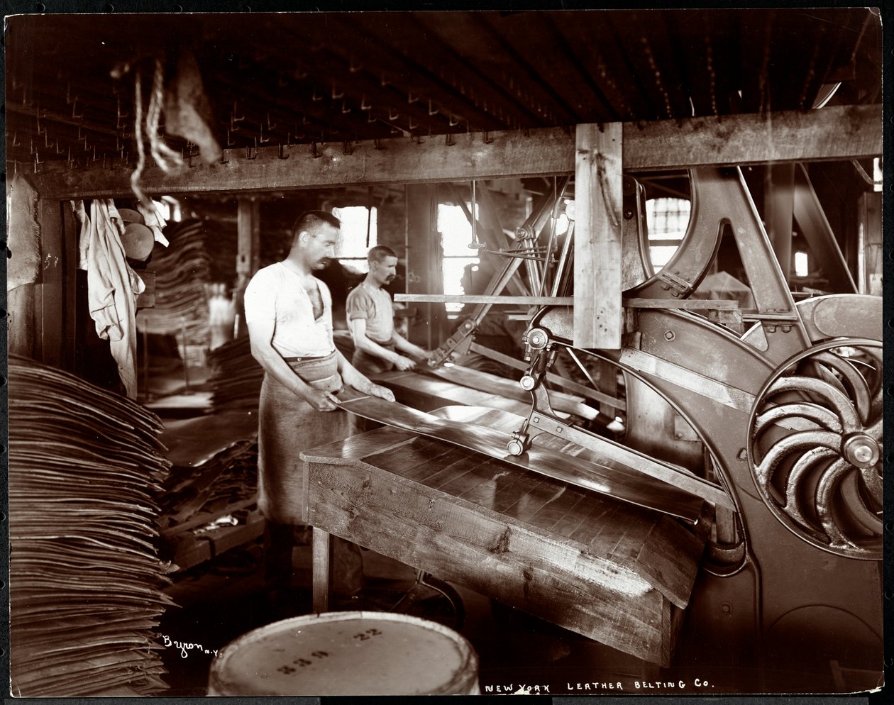 Interior view of two men working with leather and heavy equipment at the New York Leather Belting Co., New York, 1905 by Byron Company